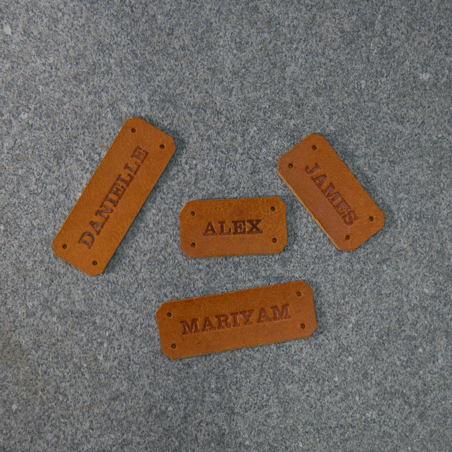 Collection of embossed name tags in Golden Brown leather with holes in each corner