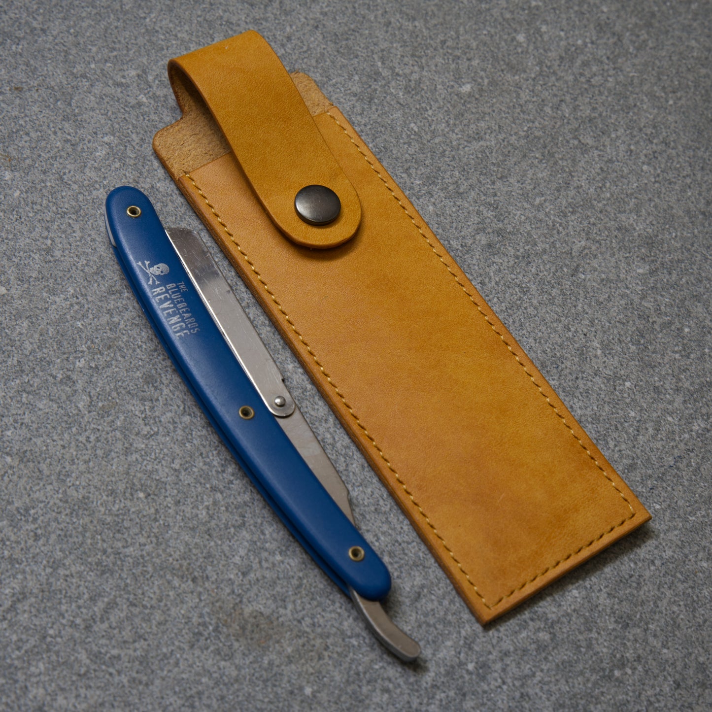 Blue straight razor with yellow leather sheath on a grey surface