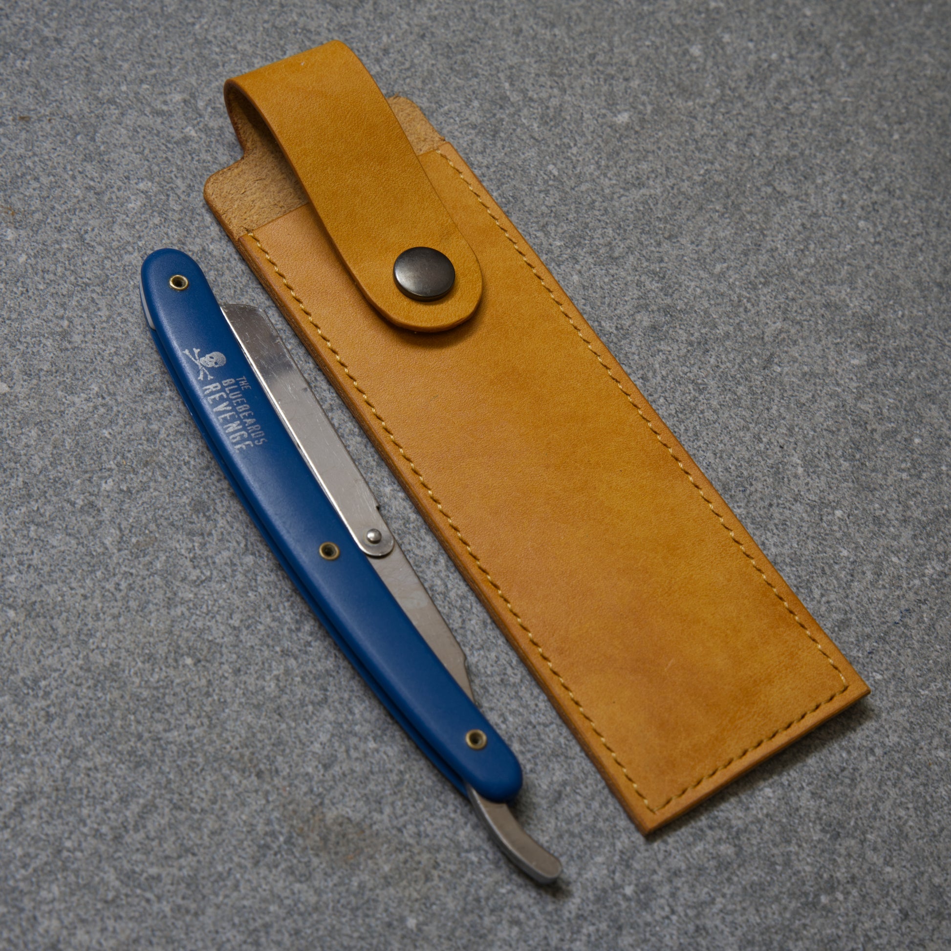 Blue straight razor with yellow leather sheath on a grey surface