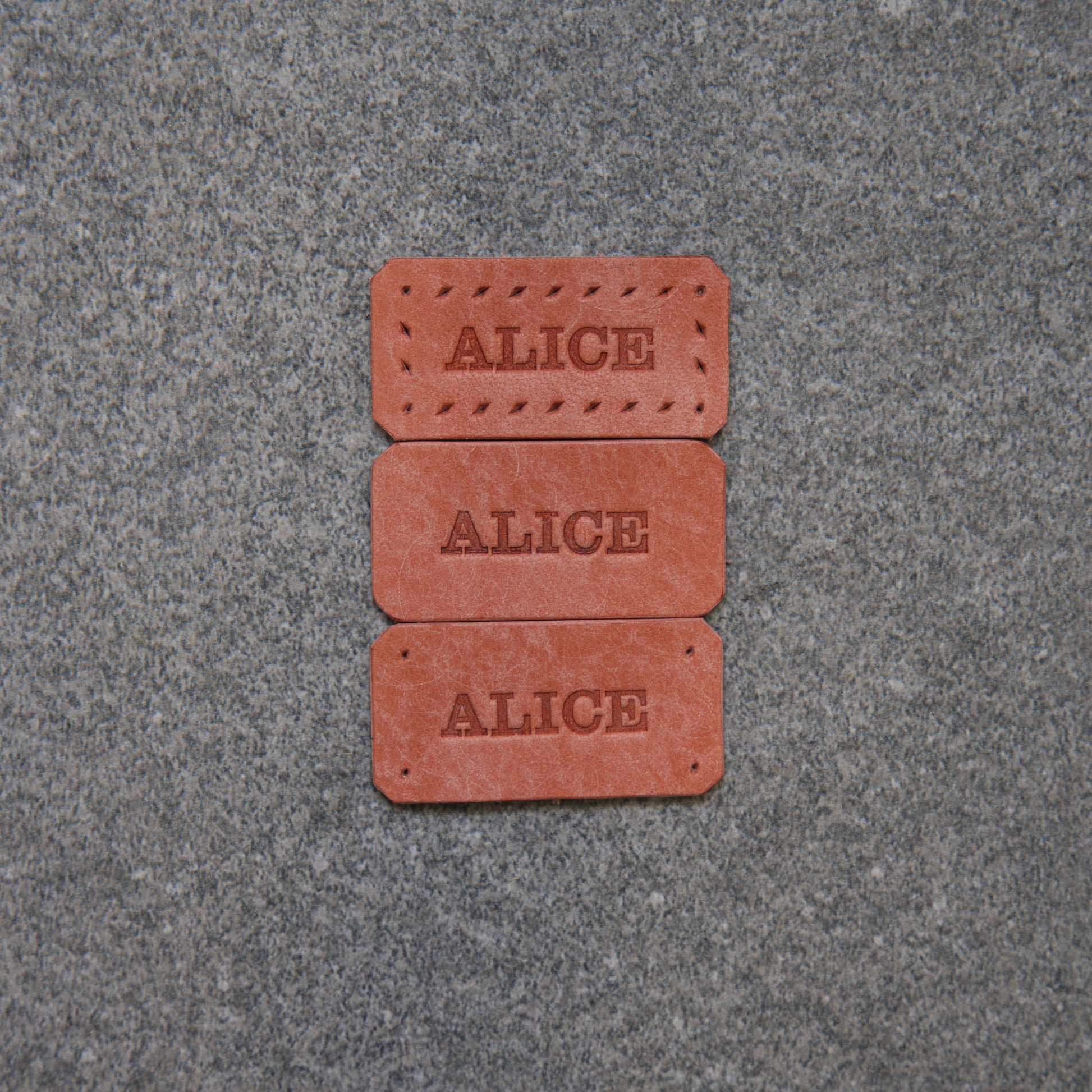 Three red rectangular bricks with 'ALICE' engraved on them, placed on a gray pavement.
