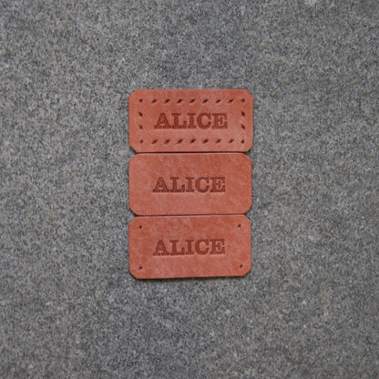 Three red rectangular bricks with 'ALICE' engraved on them, placed on a gray pavement.