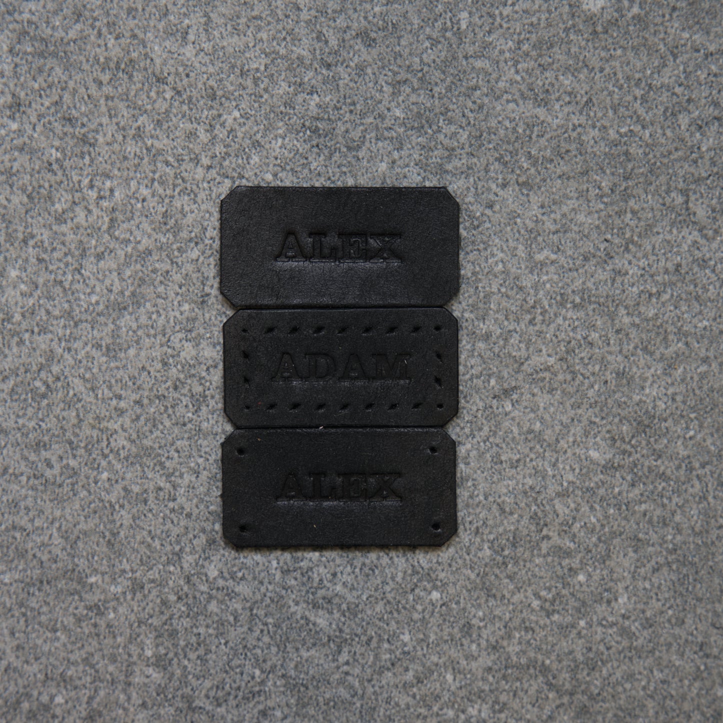 Three black nameplates with engraved names on a gray pavement