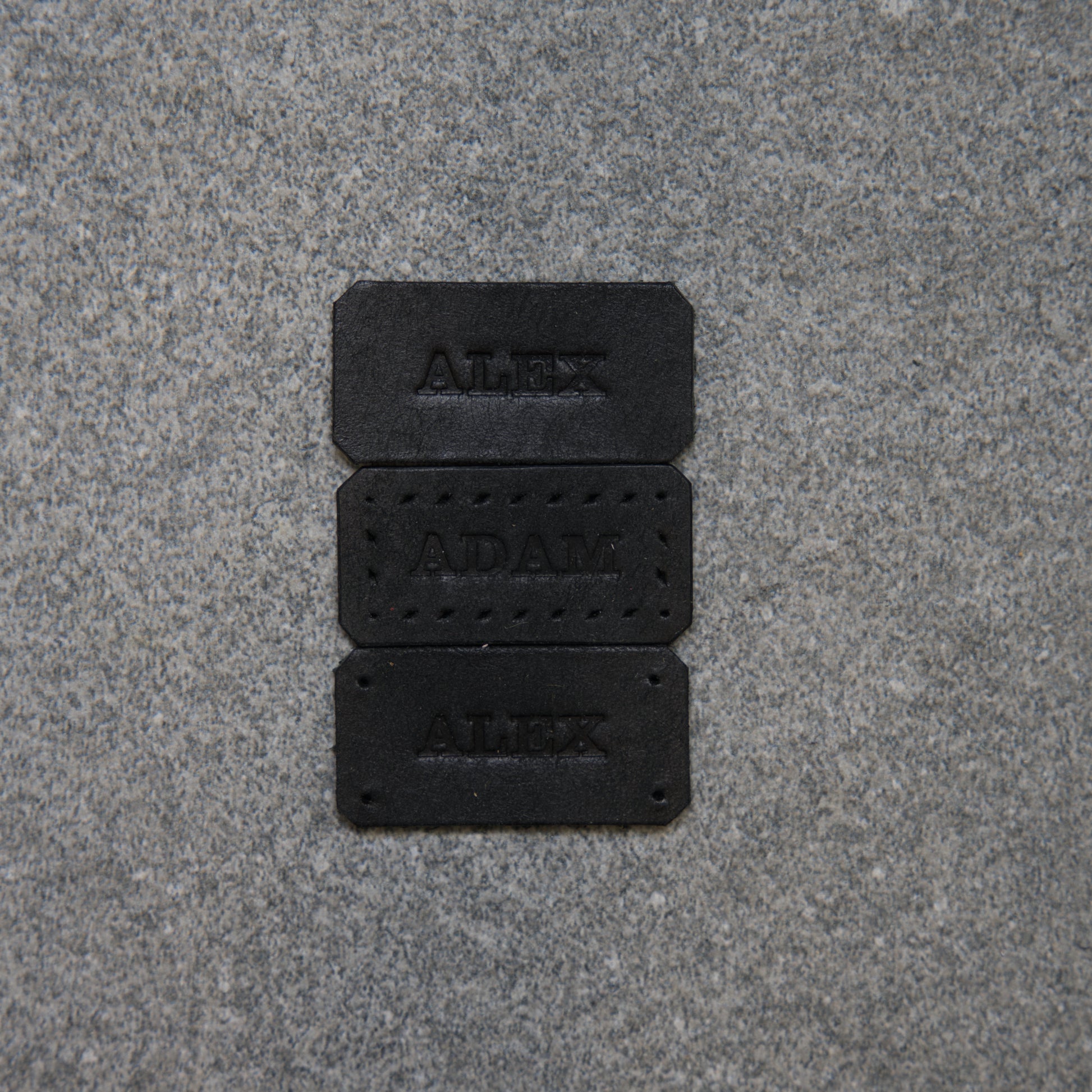 Three black nameplates with engraved names on a gray pavement