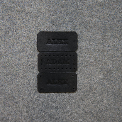 Three black nameplates with engraved names on a gray pavement