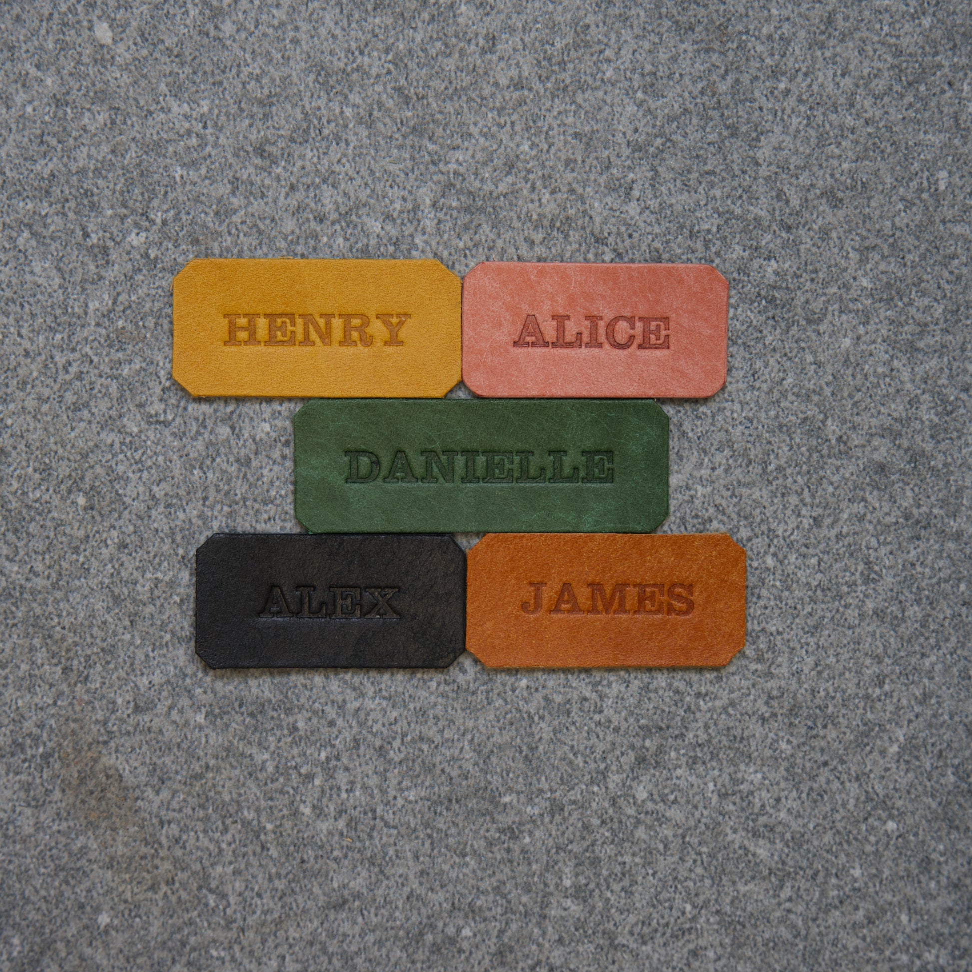 Five rectangular nameplates with names engraved on them, placed on a textured gray surface.
